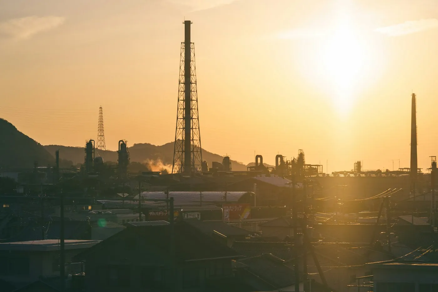 Refinery smokestacks silhouetted against an orange sky