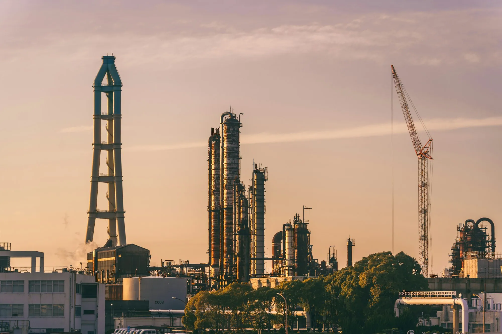 Refinery towers silhouetted against a vivid orange sky